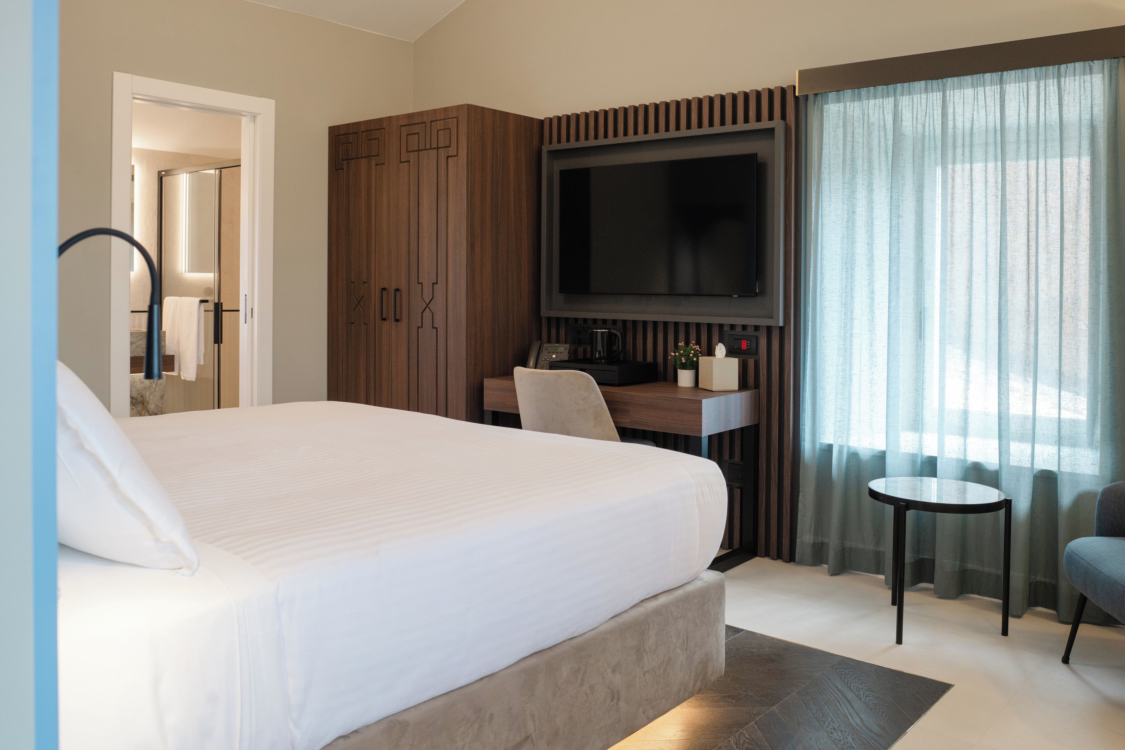 Ein Hotelzimmer mit einem großen Bett, einem an der Wand befestigten Fernseher, einem Schreibtisch mit Stuhl und einem kleinen Tisch.