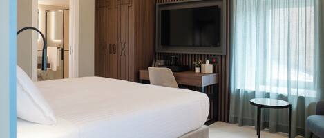 Ein Hotelzimmer mit einem großen Bett, einem an der Wand befestigten Fernseher, einem Schreibtisch mit Stuhl und einem kleinen Tisch.