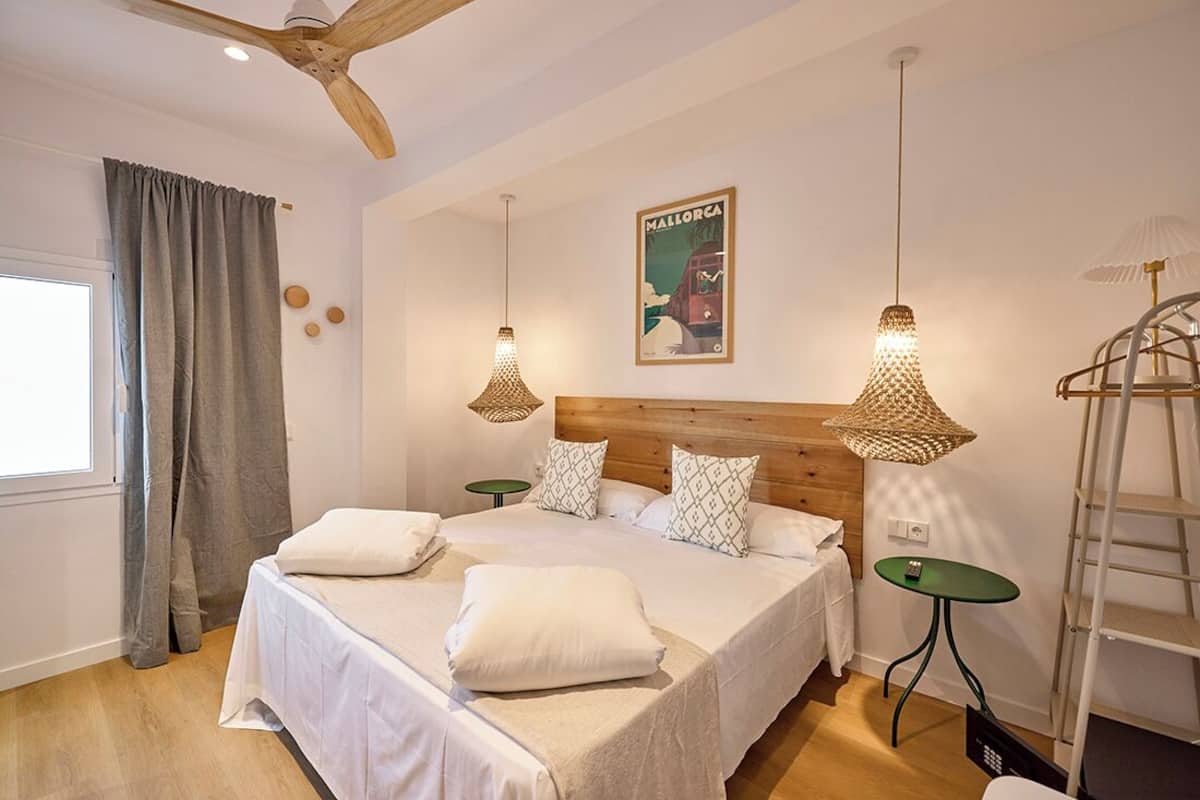 A bedroom with a large bed, two bedside tables, a ceiling fan, and a wall-mounted lamp.