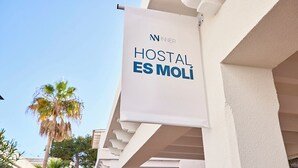 Segnale per 'HOSTAL ES MOLÍ', con una chiara vista dell'architettura dell'edificio e palme sullo sfondo.