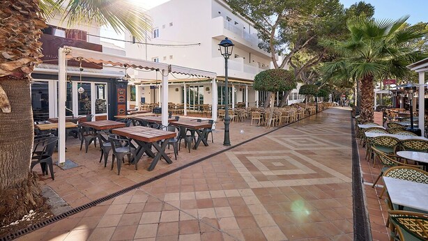 Un'area caffè all'aperto con tavoli e sedie, un vialetto piastrellato e un edificio con balconi.