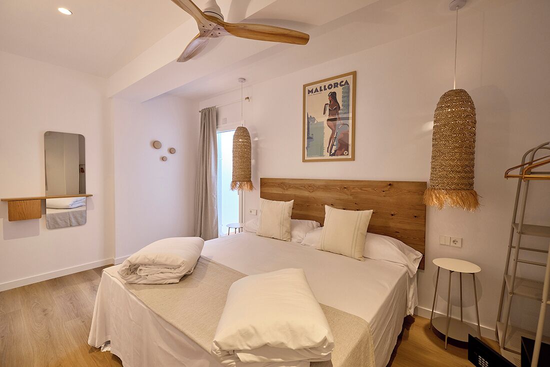 A bedroom with a large bed, wooden headboard, ceiling fan, and a poster on the wall.
