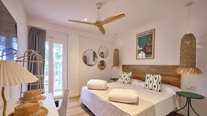 Una camera d'albergo con un letto, una ventola a soffitto, un tavolo con cappelli, una sedia e un quadro appeso al muro.