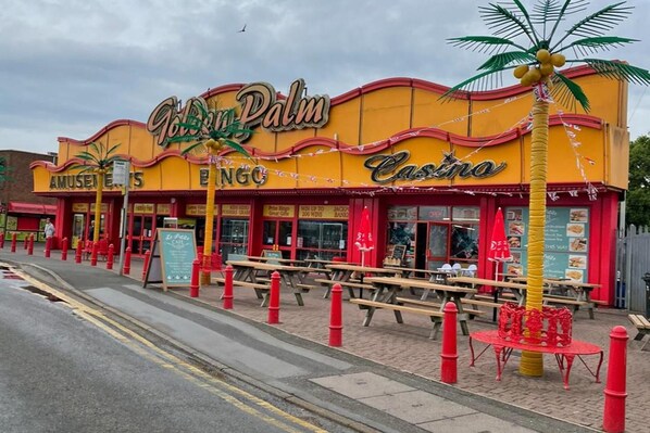 A building with a yellow facade, palm trees, and outdoor seating.