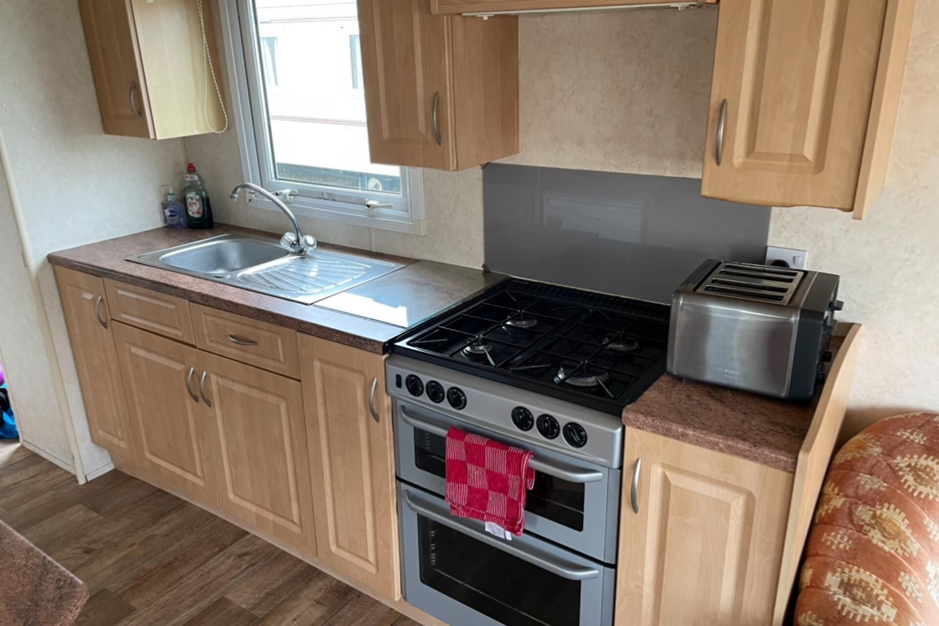 A compact kitchen with wooden cabinets, a stainless steel stove, a toaster, and a window above the sink.