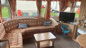 Un salon confortable avec un canapé, un téléviseur, une petite table et un fauteuil.