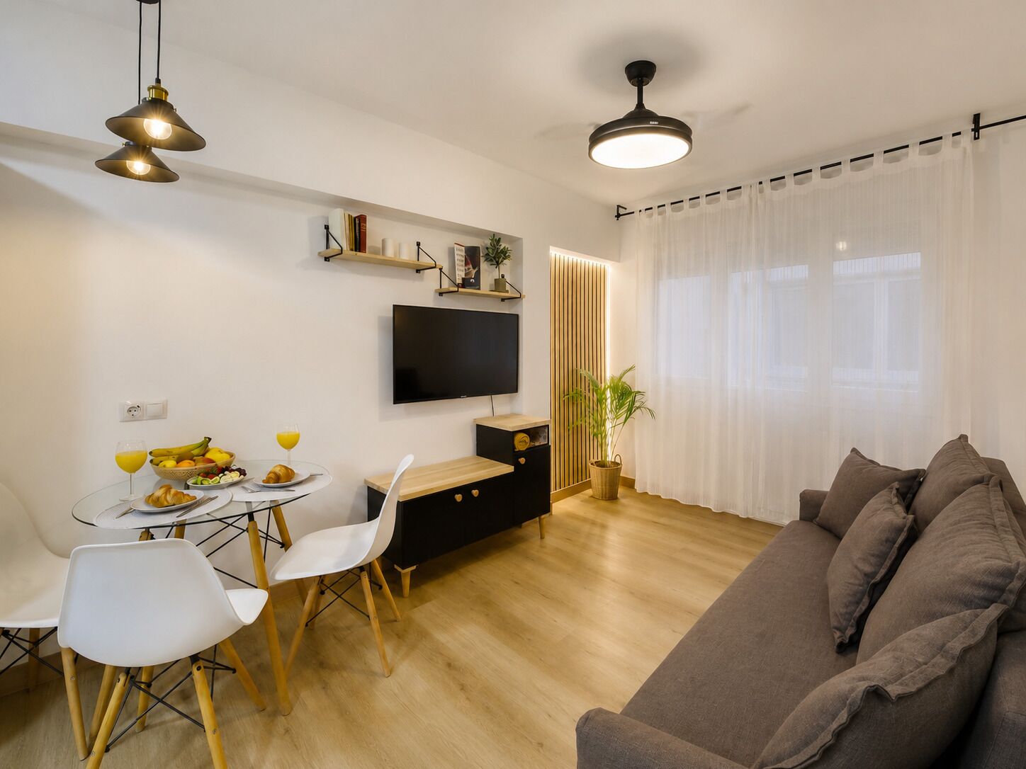 Ein modernes Wohnzimmer mit Flachbildfernseher, einer Essecke mit Tisch und Stühlen, einer Couch und einem Deckenventilator.