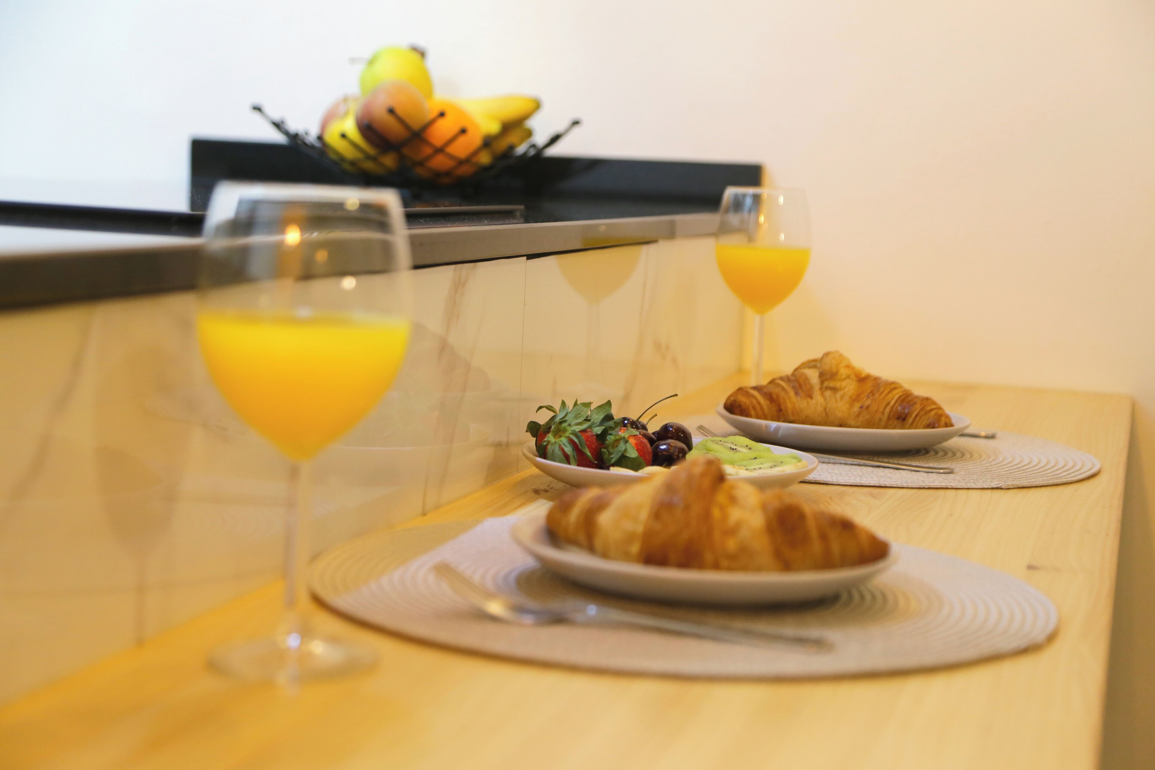 A breakfast table with croissants, fruit, and orange juice glasses.