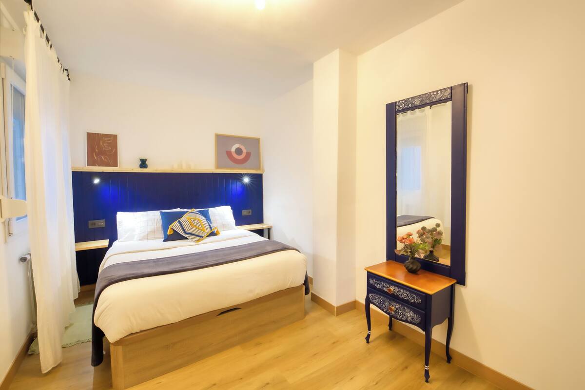 A bedroom with a bed, bedside table, and a mirror.