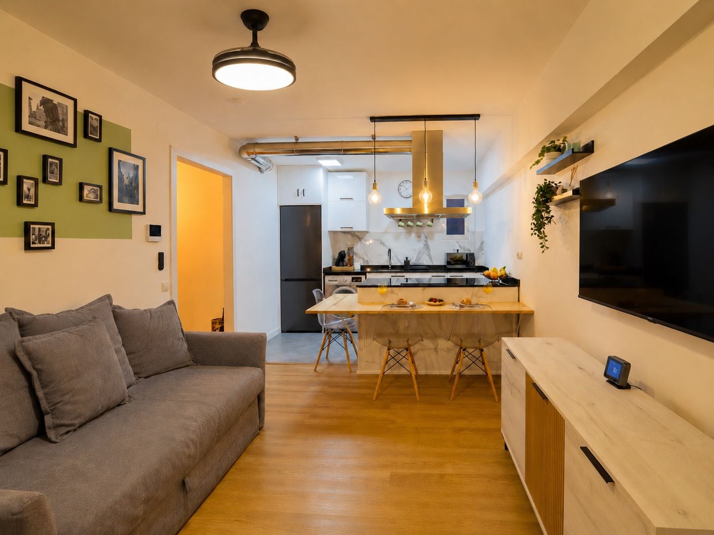 Una cuina moderna amb una illa central, una zona de menjador amb un sofà i un televisor de pantalla plana fixat a la paret.