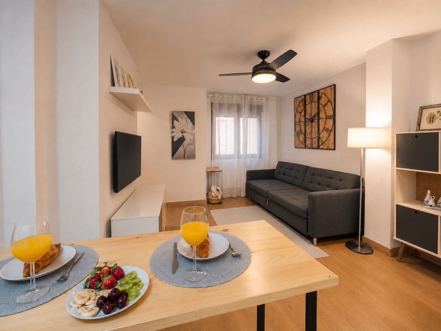 A modern living room with a sofa, a dining table with breakfast, a TV, and artwork on the walls.