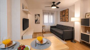 A modern living room with a sofa, a dining table with breakfast, a TV, and artwork on the walls.