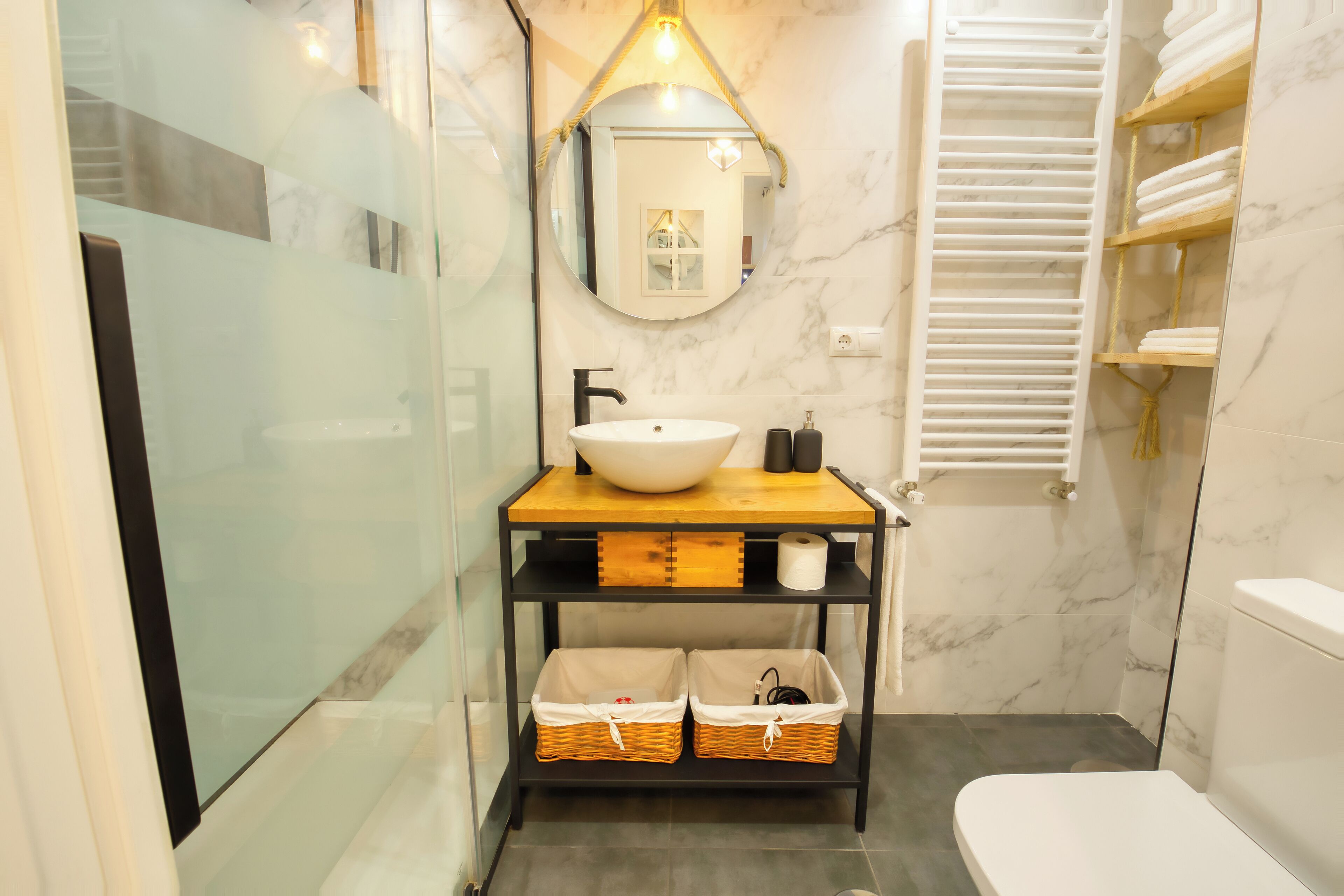 A modern bathroom with a glass shower enclosure, a white sink, and a wooden vanity with baskets.