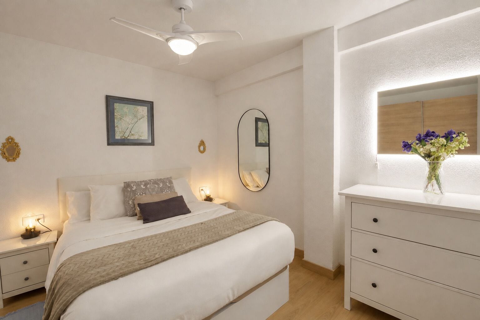 A bedroom with a bed, bedside tables, a dresser, a ceiling fan, a wall-mounted mirror, and a framed picture.