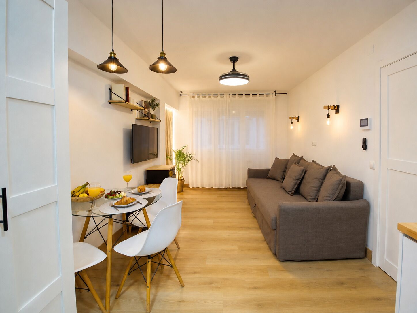 A compact living space with a dining area, a sofa, and a TV mounted on the wall.