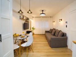 Un espacio habitable compacto con comedor, sofá y televisor fijado a la pared.