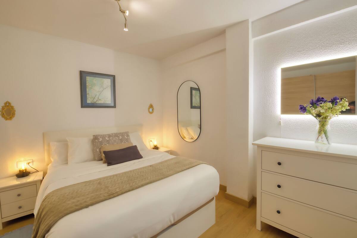 A neatly arranged bedroom with a bed, bedside tables, a dresser, and a mirror.