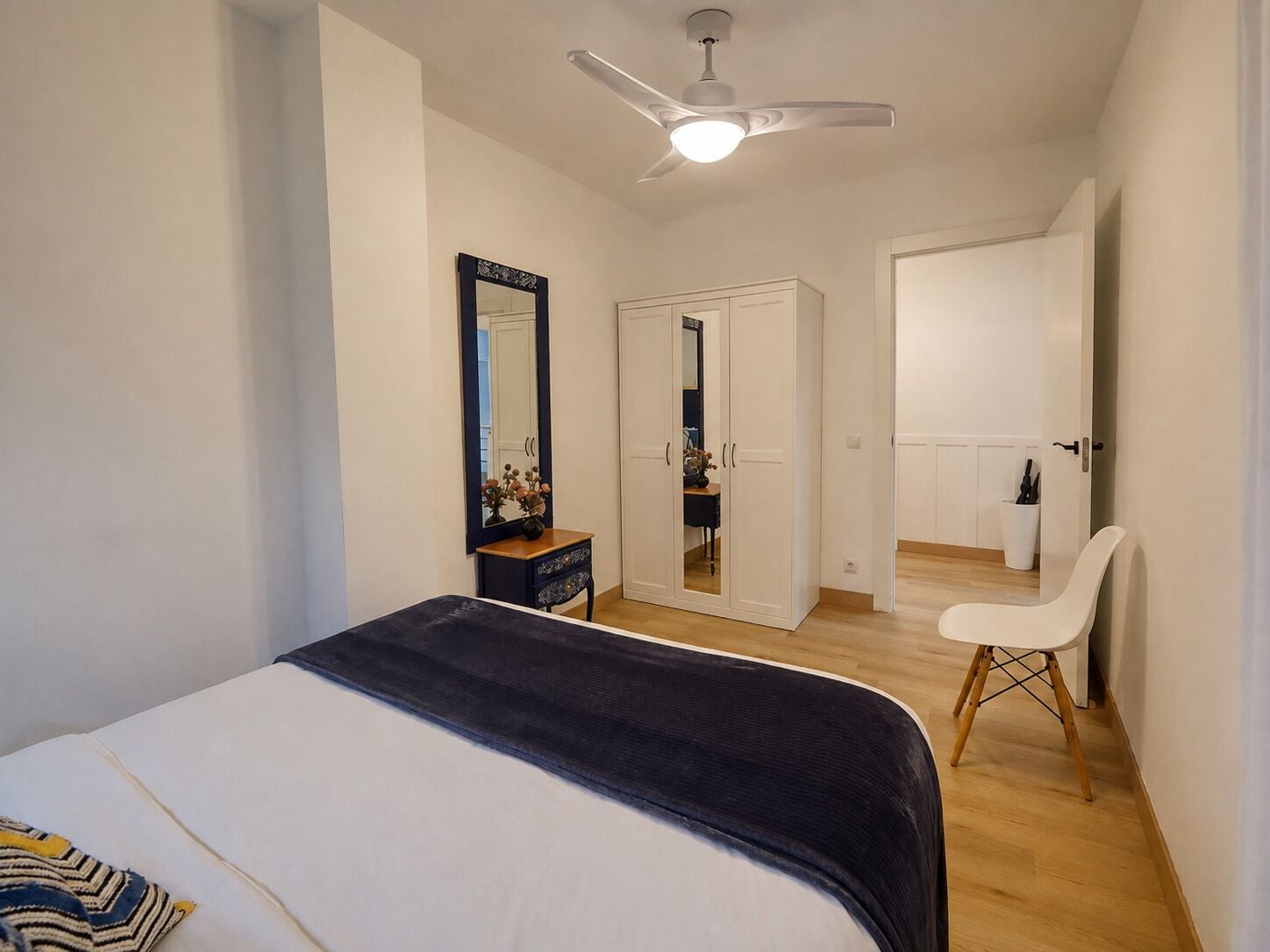 A bedroom with a bed, a dresser, a mirror, a wardrobe, a chair, and a ceiling fan.