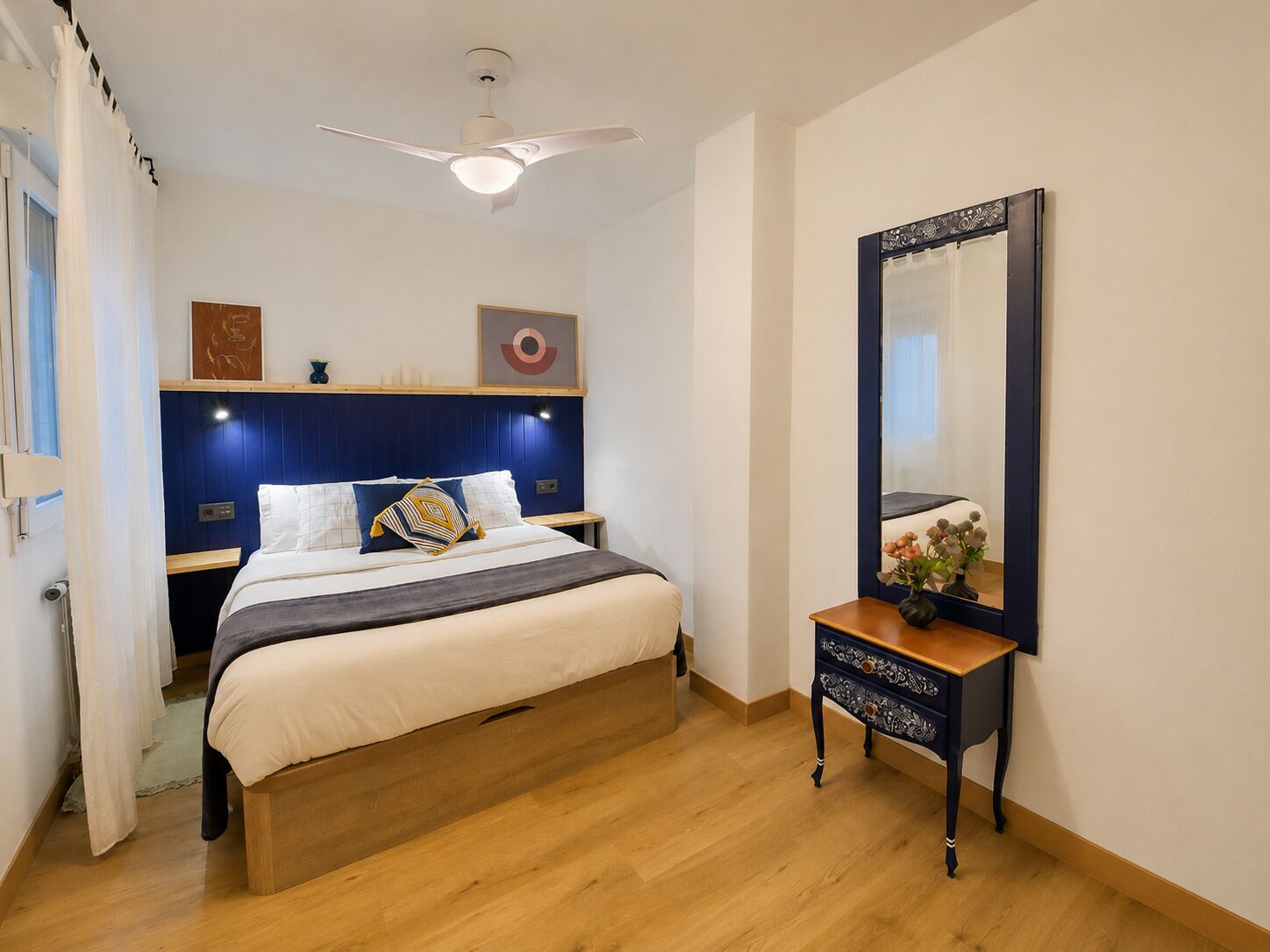 Ein Schlafzimmer mit Bett, Nachttisch, Spiegel und Deckenventilator.