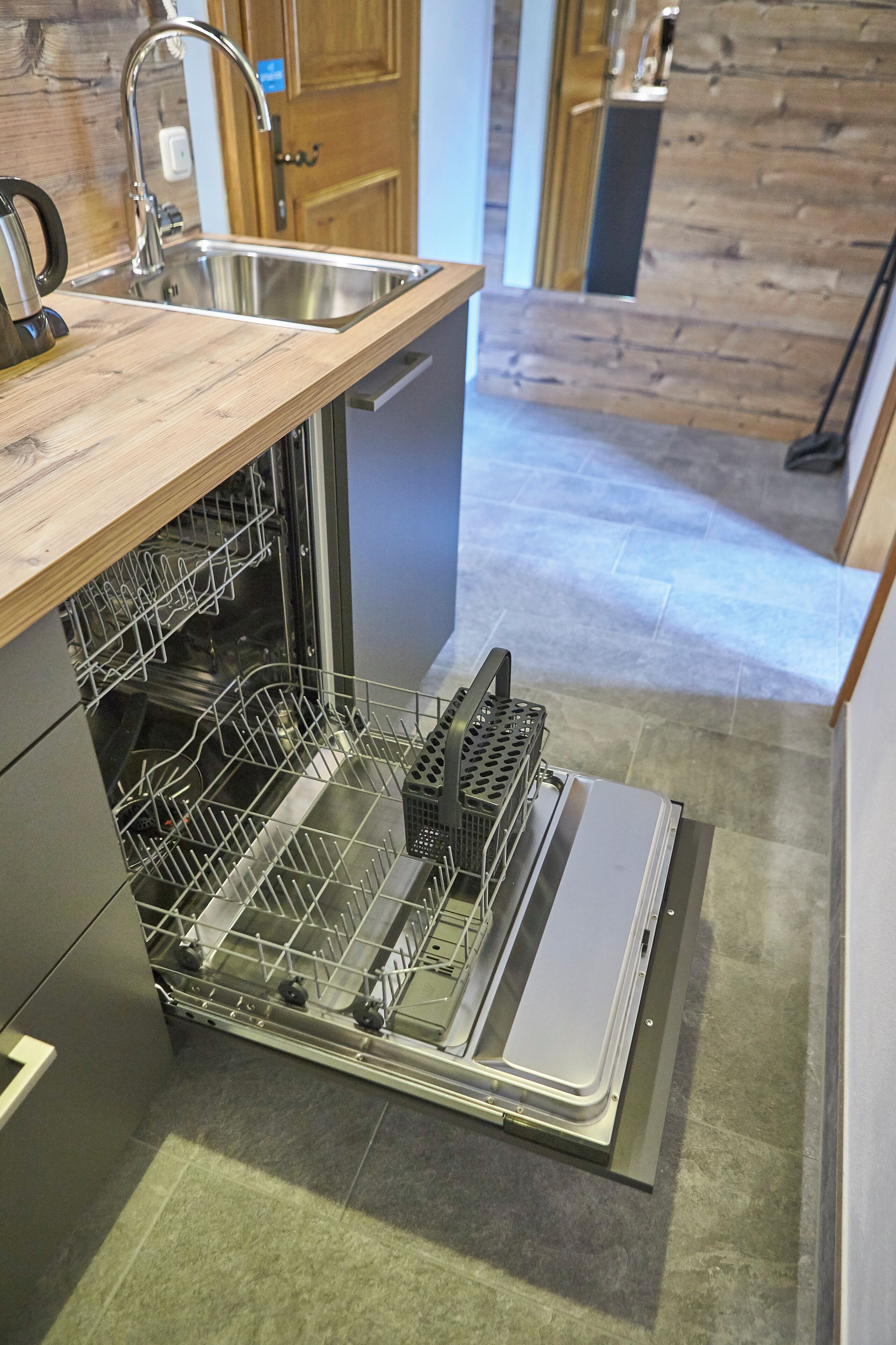 Cocina compacta con lavavajillas, encimera de madera y pileta de acero inoxidable.