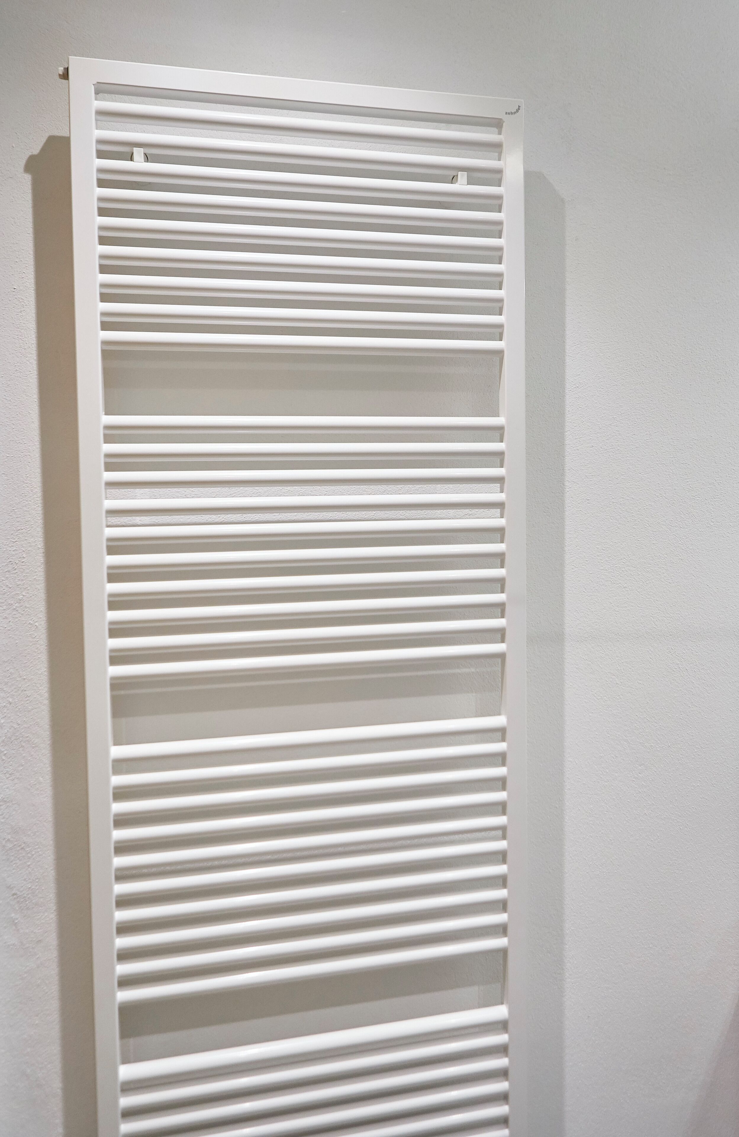 A white, vertical, wall-mounted radiator with horizontal slats.