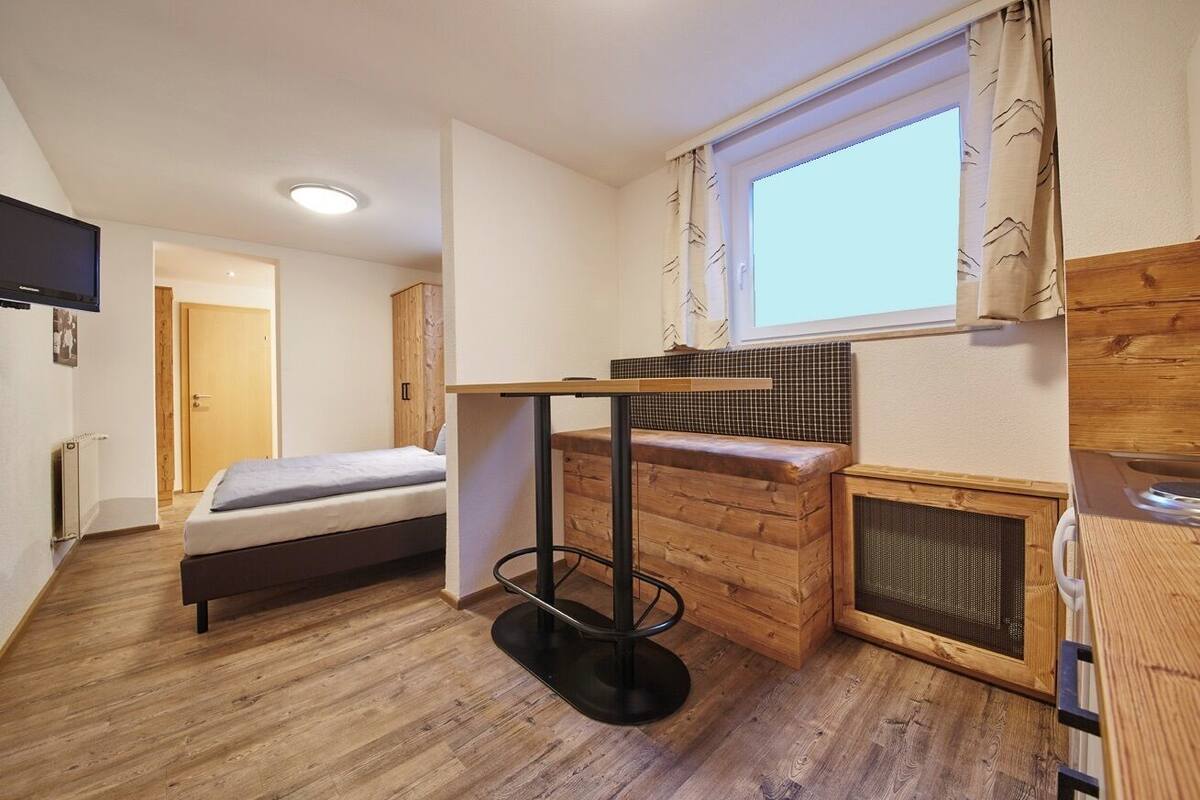 A compact room with a bed, a small table, a window, and a radiator.