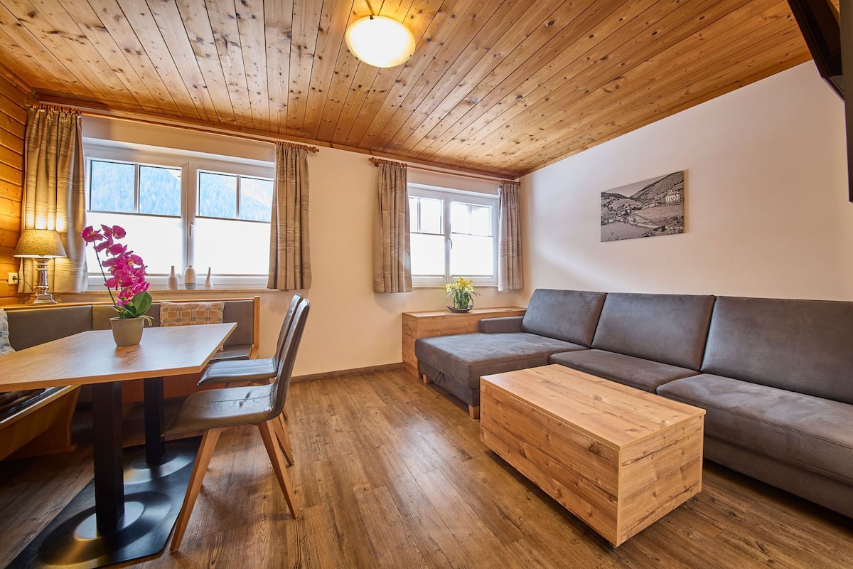 A cozy living room with a wooden ceiling, a sofa, a dining table with chairs, and a coffee table.