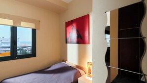 A bedroom with a bed, a bedside table, a mirror, and a window.
