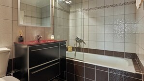 A bathroom with a bathtub, a sink with a red countertop, and a mirror above the sink.