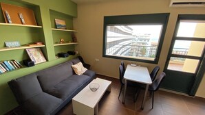 A compact living space with a sofa, a small table, and a window offering a view of a building.
