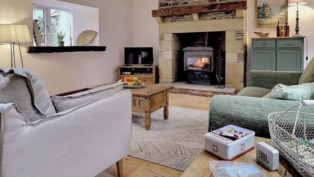 Un salon chaleureux avec une cheminée en pierre, des poutres en bois, un téléviseur et des sièges confortables.