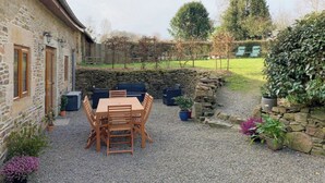 Un bâtiment en pierre avec une terrasse en gravier, une table et des chaises en bois, et des plantes en pot.