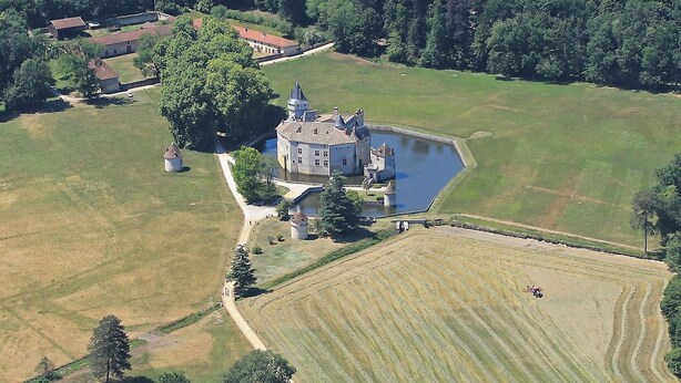 Luchtbeeld van een kasteel met een gracht, omringd door velden en bebost gebied.