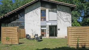 Een modern huis met twee verdiepingen, een overdekt terras, een kleine tuin en een houten omheining.
