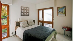 Een slaapkamer met een bed, nachtkastje, lamp, raam en schilderij.
