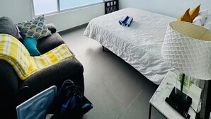 Ett modernt sovrum med en stor säng, en soffa, ett bord med en lampa, ett fönster och en taklampa.