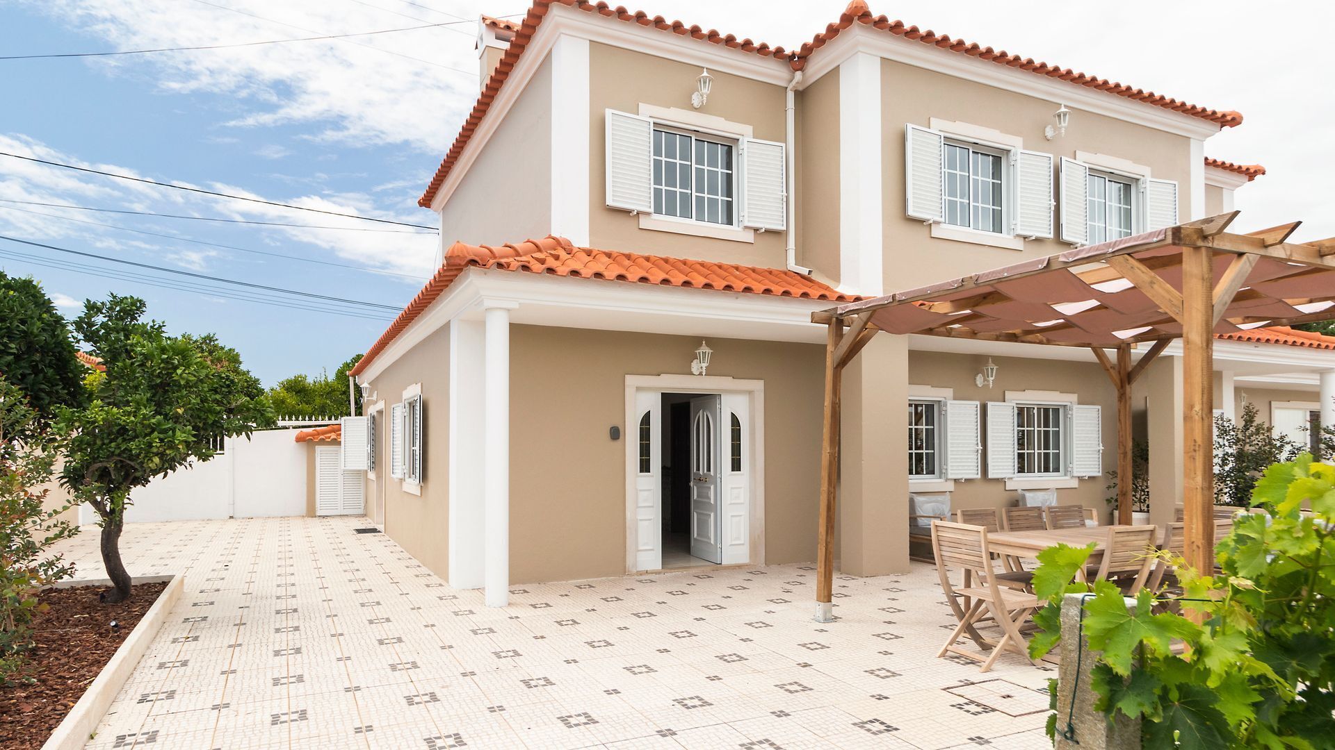 A two-story house with a tiled patio, a pergola, and a small garden.