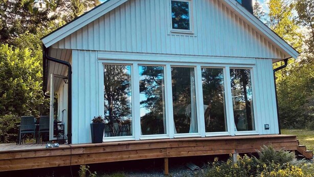 Una baita di legno bianco con ampie finestre, un portico e un camino.