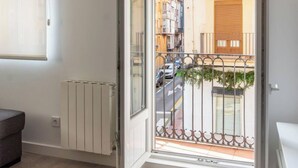 A room with a radiator, a door leading to a balcony with a metal fence, and a view of a street with buildings. - Apartamento Atalaya en el centro (Santander)