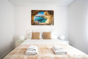 Een hotelkamer met een bed, twee kussens, een nachtkastje, een lamp en een schilderij van een kustlandschap.