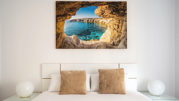 Een slaapkamer met een bed, twee kussens, een nachtkastje en een schilderij van een kustlandschap aan de muur.