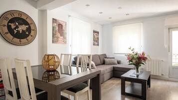A modern living room with a large wall clock, a sofa, a dining table, and a window with natural light.