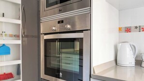 A kitchen with a built-in oven and microwave, a kettle, and a shelf with cleaning supplies. - Apartamento Atalaya en el centro (Santander)