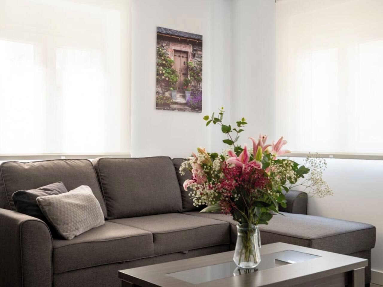 Una sala moderna con un sofá gris, una mesa de centro de vidrio y un jarrón de flores.