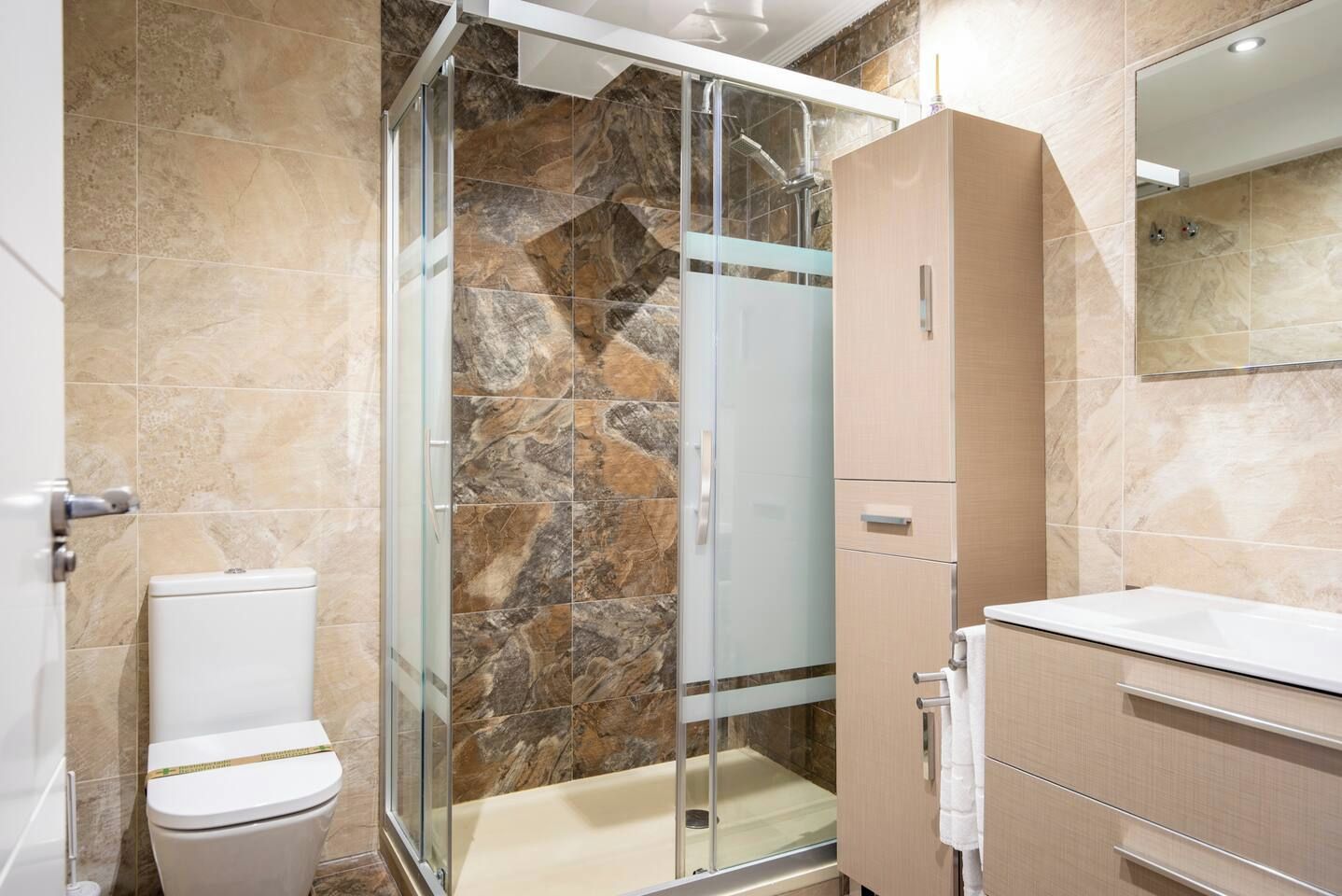 A bathroom with a glass shower enclosure, a toilet, a sink, and a mirror.