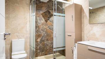 A bathroom with a glass shower enclosure, a toilet, a sink, and a mirror.