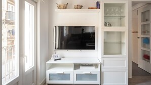 Een moderne woonkamer met een grote flatscreen televisie aan een witte muur, een glazen salontafel en inbouwkasten met glazen deuren.