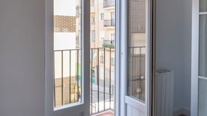 Een kamer met een grote schuifglazen deur die leidt naar een balkon met uitzicht op een woongebouw.