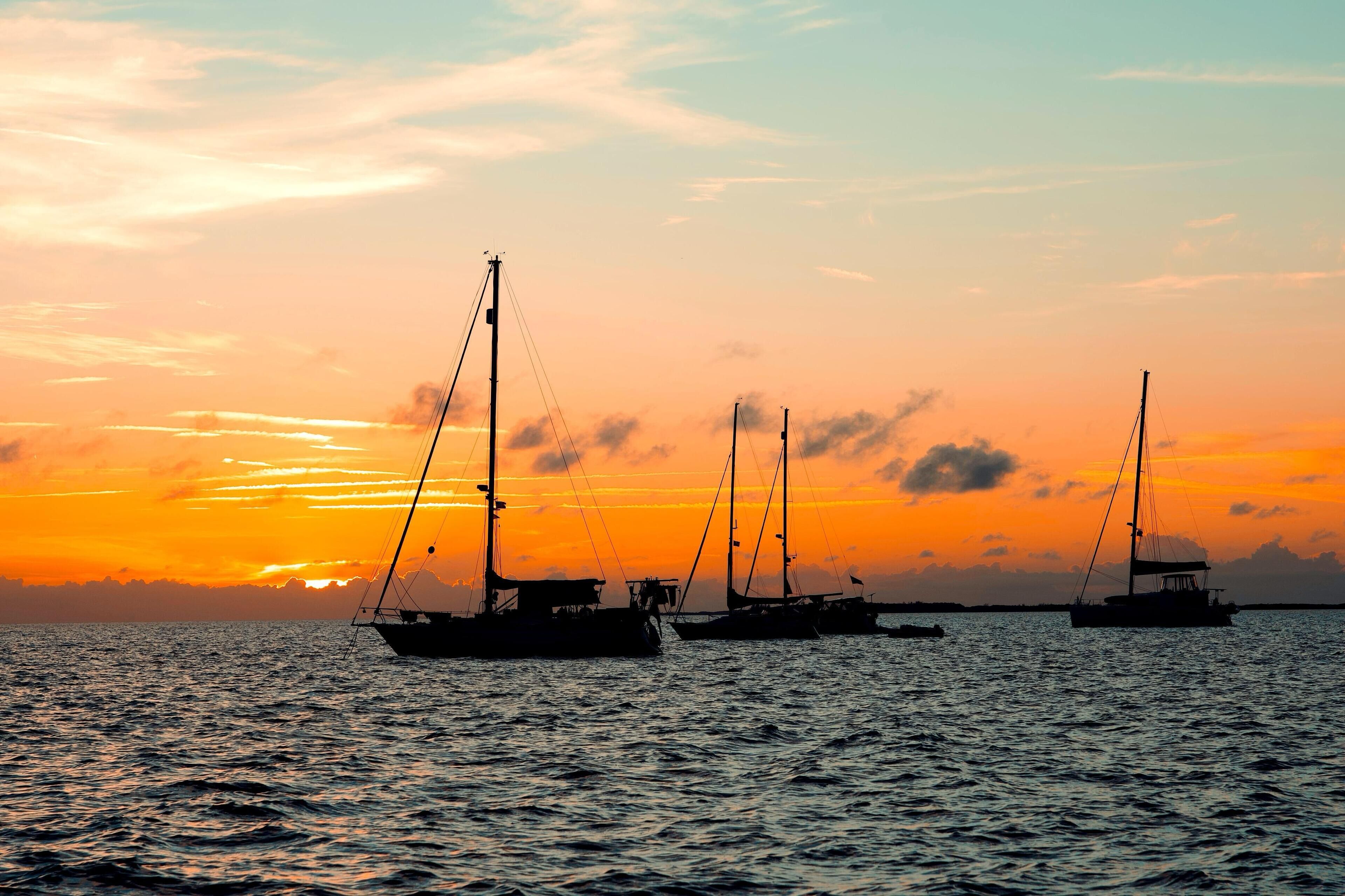Un coucher de soleil sur une mer calme, avec plusieurs voiliers ancrés.