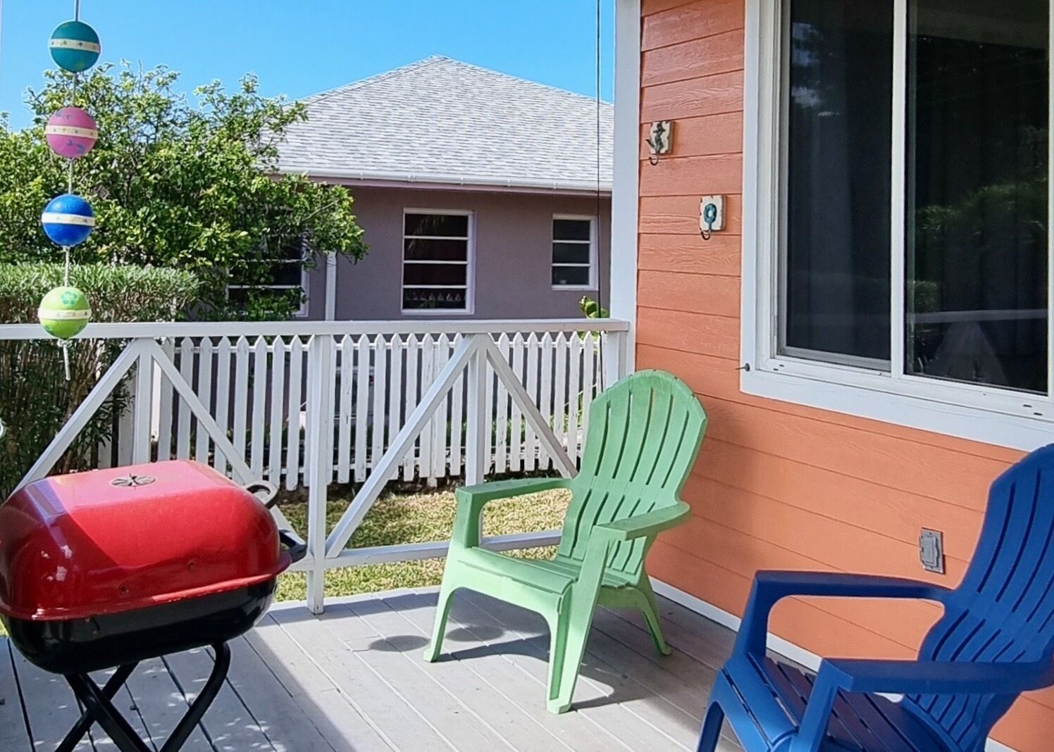 A deck with a barbecue grill, two green chairs, and a blue chair.